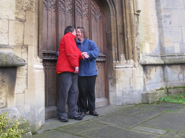 A photograph of two people hugging outside a church