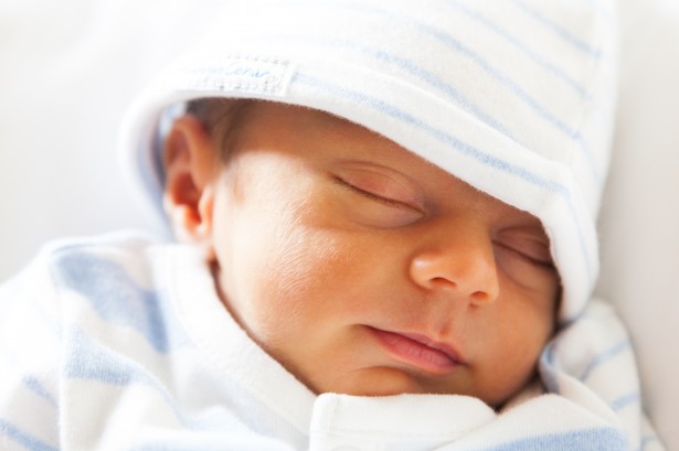 A photo of a sleeping baby with a blue and white striped hat on.